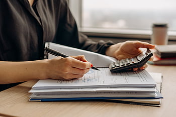 Close-up of person using a calculator with financial documents in an office. HD wallpaper