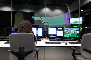 Female engineer managing multiple screens during a technology simulation in a control room. HD wallpaper