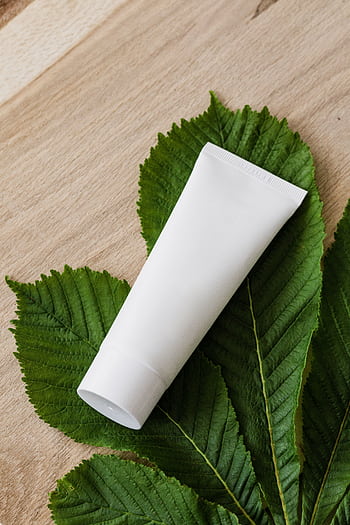 White cosmetic tube on lush green leaves promoting natural skincare. HD phone wallpaper