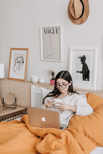 A woman relaxing in bed with coffee and laptop, surrounded by art and comfort. HD phone wallpaper