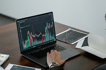 A person analyzing stock market data on a laptop with charts and graphs visible. HD wallpaper