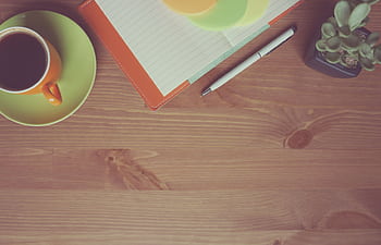 A warm-toned workspace with a cup of coffee, notebook, pen, and succulent on a wooden table. HD wallpaper