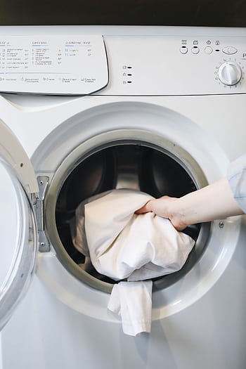 Close-up of a person's hand putting laundry into a front-loading washing machine. HD phone wallpaper