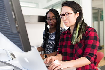 Two women working on a computer project together in an office setting. HD wallpaper