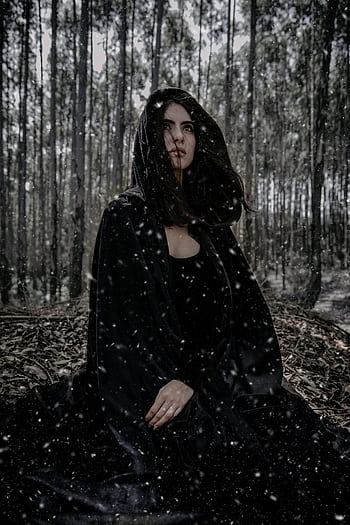 A mysterious woman sits in a snowy winter forest, dressed in a dark cloak. HD phone wallpaper
