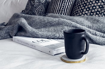 A cozy interior scene featuring a black mug, a book, and patterned pillows on a soft couch. HD wallpaper