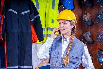 Woman engineer in safety gear with braided hair talks on in industrial setting. HD wallpaper