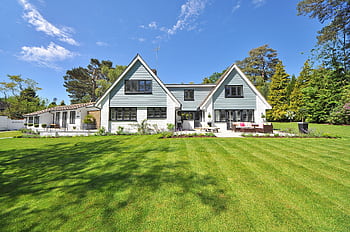 Modern family home exterior showcasing a large lawn and garden under a clear blue sky. HD wallpaper