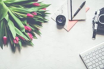 A beautifully arranged workspace featuring tulips, a vintage camera, and elegant stationery items. HD wallpaper