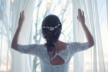 Beautiful bride in lace dress looks out a sunlit window, capturing a moment of serene elegance. HD wallpaper