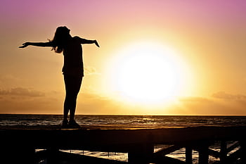 A joyful silhouette of a woman standing on a dock at sunset, embracing the dom of nature. HD wallpaper