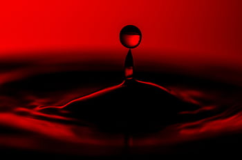 Close-up capturing the dramatic splash of a water drop on a vivid red background. HD wallpaper
