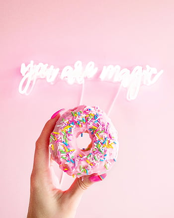 Vibrant donut with sprinkles held against a pink background and neon 'you are magic' sign. HD phone wallpaper