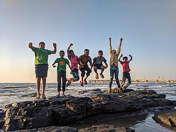 Group of kids joyfully jumping on rocks by the seaside. Fun and playful moment captured outdoors. HD wallpaper