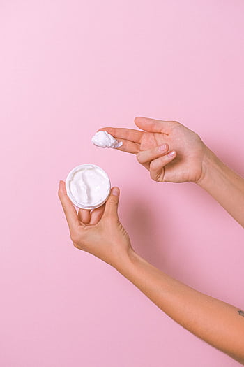Closeup of hands applying face cream from a jar on a pink background. HD phone wallpaper