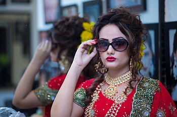 Beautiful South Asian bride in traditional red attire, adorned with jewelry and sunglasses, posing indoors. HD wallpaper