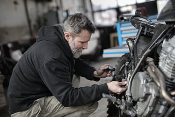 Focused mechanic working on motorcycle repair in a garage setting. HD wallpaper