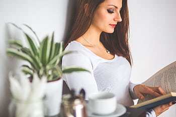 A young woman enjoys a peaceful moment reading a book indoors, near a potted plant. HD wallpaper