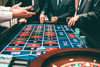 Group of people playing roulette, placing bets in a casino setting. HD wallpaper