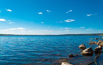 Serene view of a blue lake with rocky shore under a clear blue sky, ideal for nature lovers. HD wallpaper