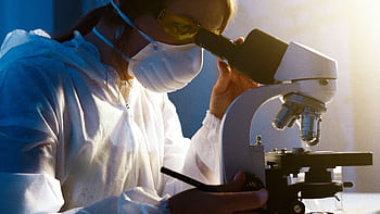 A female scientist uses a microscope in a laboratory, focusing intently on her research. HD wallpaper