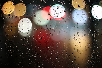 Colorful bokeh lights behind raindrop-covered windowpane, creating a vibrant and moody atmosphere. HD wallpaper