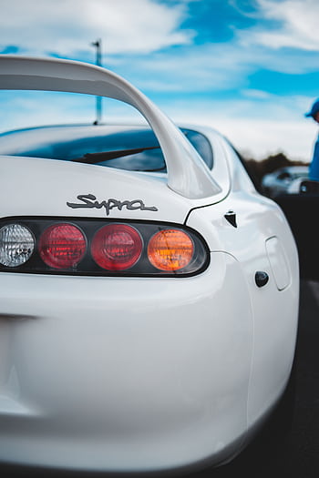 White sports car showcasing its rear design and distinctive wing spoiler, under a clear blue sky. HD phone wallpaper