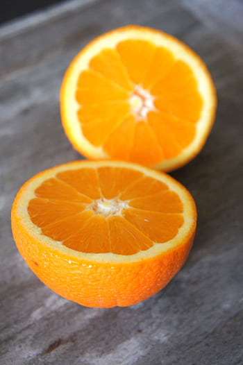 Vibrant close-up of two fresh orange slices on a rustic surface, highlighting their juicy texture. HD phone wallpaper