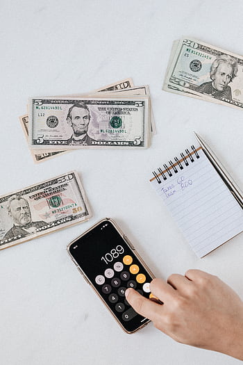 Overhead view of a hand using a calculator with US dollars and notes, representing finance and budgeting. HD phone wallpaper