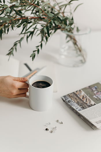 A clean and serene workspace with a white mug of coffee, surrounded by a plant, notebook, and newspaper. HD phone wallpaper