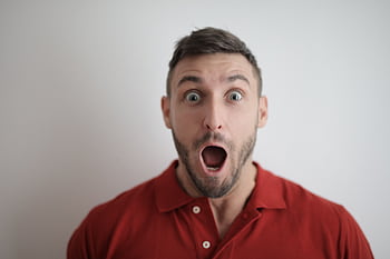 Portrait of a shocked man in a red polo shirt with a white background, expressing surprise. HD wallpaper