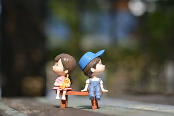 Adorable figurines of a boy and girl sit on a bench, bathed in summer sunlight. HD wallpaper