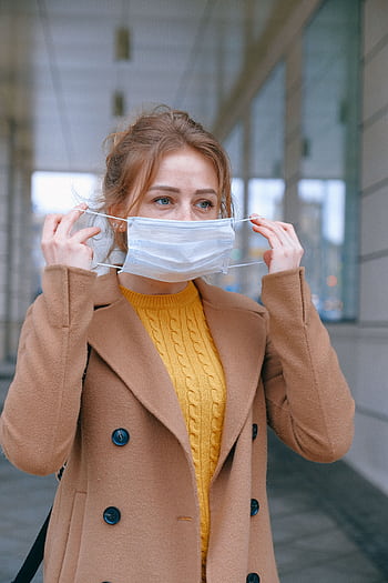 Woman adjusting her face mask on a city street, emphasizing health and protection. HD phone wallpaper