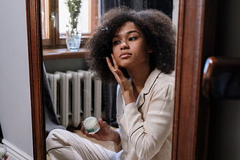 A woman applies skincare cream in a cozy home environment during her morning routine. HD wallpaper