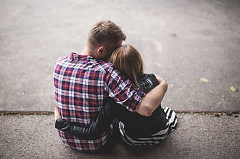 A couple sitting closely together on the ground, sharing an intimate embrace. HD wallpaper
