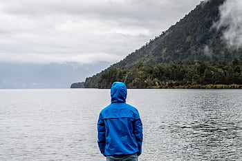 A person in a blue jacket stands by a misty New Zealand lake, surrounded by mountains. HD wallpaper