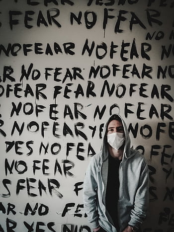 Person in a hoodie with mask stands before 'No Fear' graffiti wall, emphasizing bold expression. HD phone wallpaper