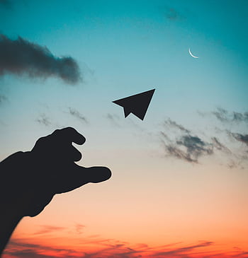 A silhouette of a hand launching a paper plane against a colorful dusk sky with a crescent moon. HD phone wallpaper