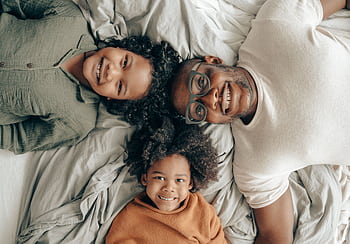 Joyful family of a father with his children enjoying a cozy moment on a bed, smiling warmly. HD wallpaper