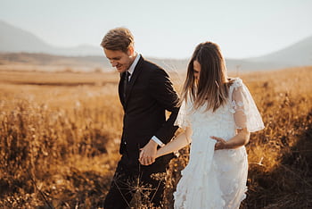 Newlywed couple walking hand in hand through a golden field on their wedding day, exuding love and happiness. HD wallpaper