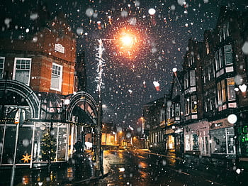 Magical night scene with snow falling on a lit urban street, capturing winter charm. HD wallpaper