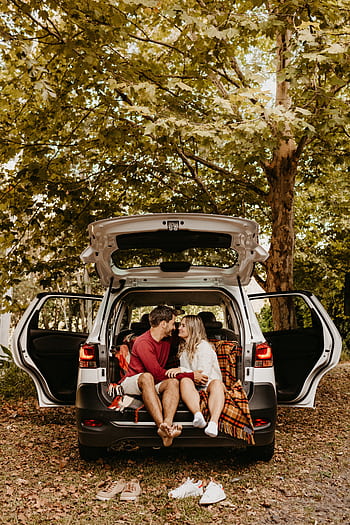 Couple sitting in the back of a car, sharing a romantic moment outdoors among lush trees. HD phone wallpaper