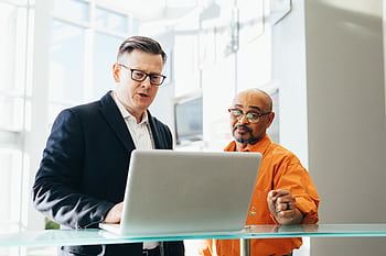 Two business professionals engaged in a collaborative discussion over a laptop in a modern office setting. HD wallpaper