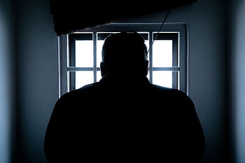 Dark silhouette of a man in a prison cell, backlit by window bars. HD wallpaper