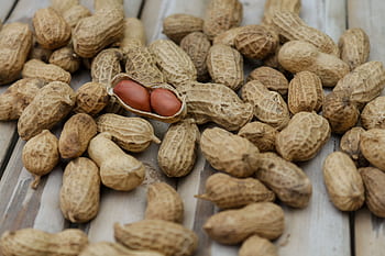 A detailed close-up of peanuts in their shells scattered on a wooden surface. HD wallpaper