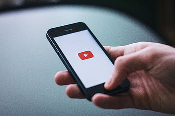 Close-up of a hand holding a smart displaying the YouTube app on the screen. HD wallpaper