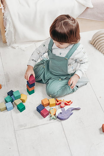 A young child sitting indoors, playing with colorful wooden blocks and toys, focused on building. HD phone wallpaper