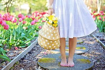 A woman in a white dress carries a basket of yellow flowers while walking barefoot in a tulip garden. HD wallpaper