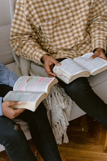 Two individuals sitting on a sofa reading and discussing the Bible indoors. HD phone wallpaper