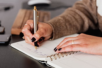 Close-up of woman writing in a spiral notebook at a desk. Perfect for work and lance themes. HD wallpaper